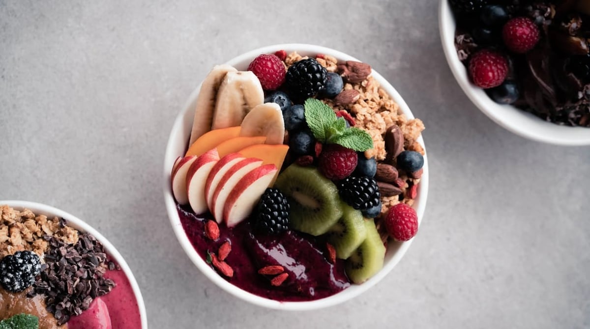 Zwei Smoothie Bowls mit Beeren, Banane, Kiwi und Granola in weißen Schalen