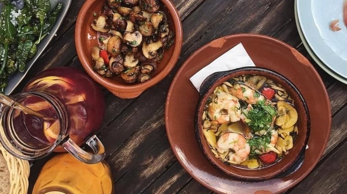 Tapas auf einem dunklen Holztisch, darunter Pilze und Garnelen in Tonschalen