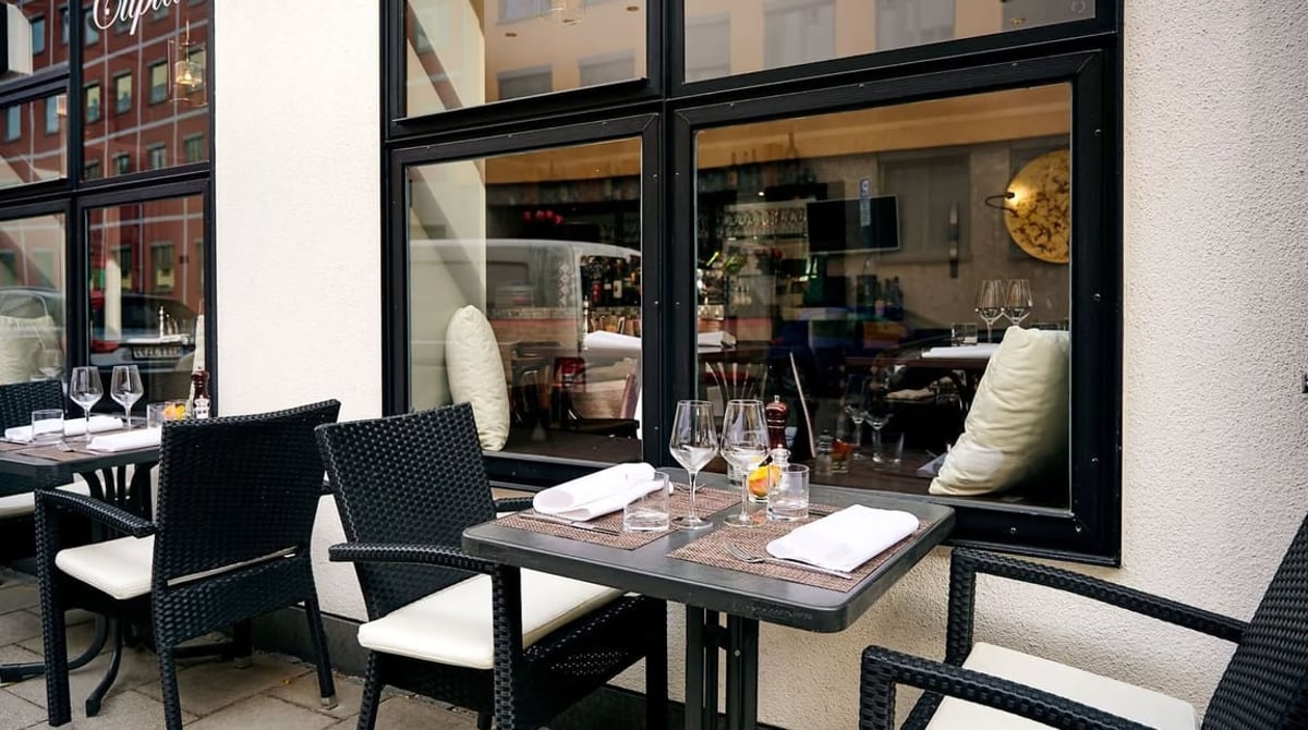 Gedeckte Tische an der Straßenterrasse des Cupido vor dem Schriftzug am Fenster