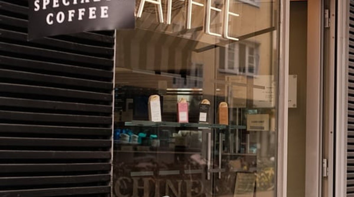 Eingang des Cafés in der Hohenzollernstraße mit Specialty-Coffee-Fahne und Krokodil auf der Scheibe