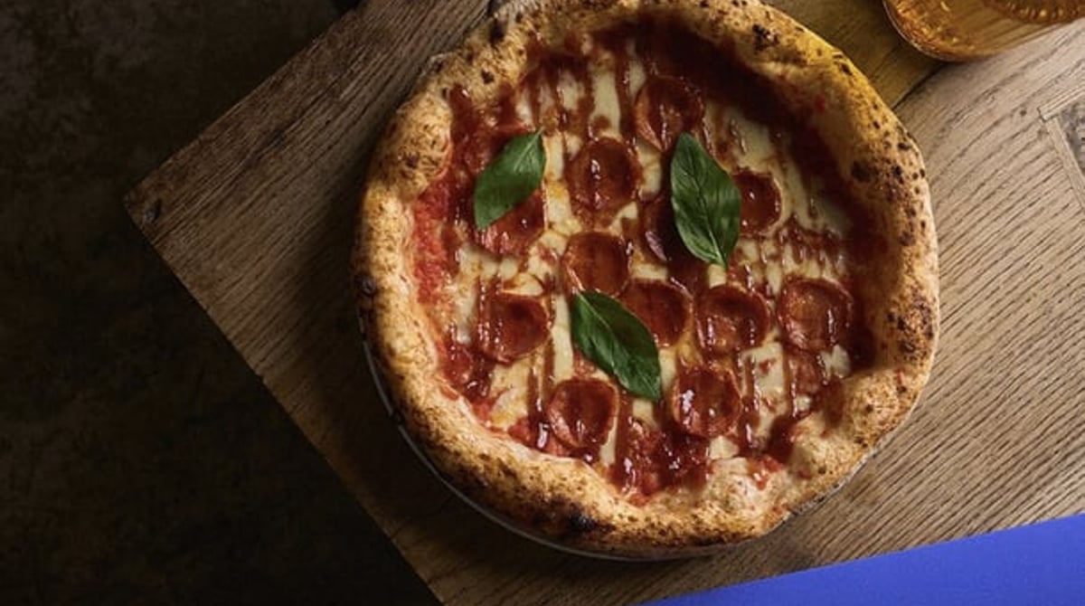 Pizza mit Salami und Basilikum auf dem Holztisch neben der blauen Speisekarte