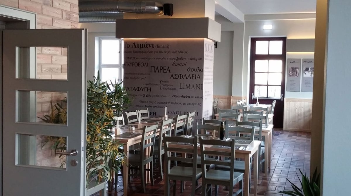 Gastraum der Taverna Limani mit gedeckten Tischen, Backsteinwand und Fenstern