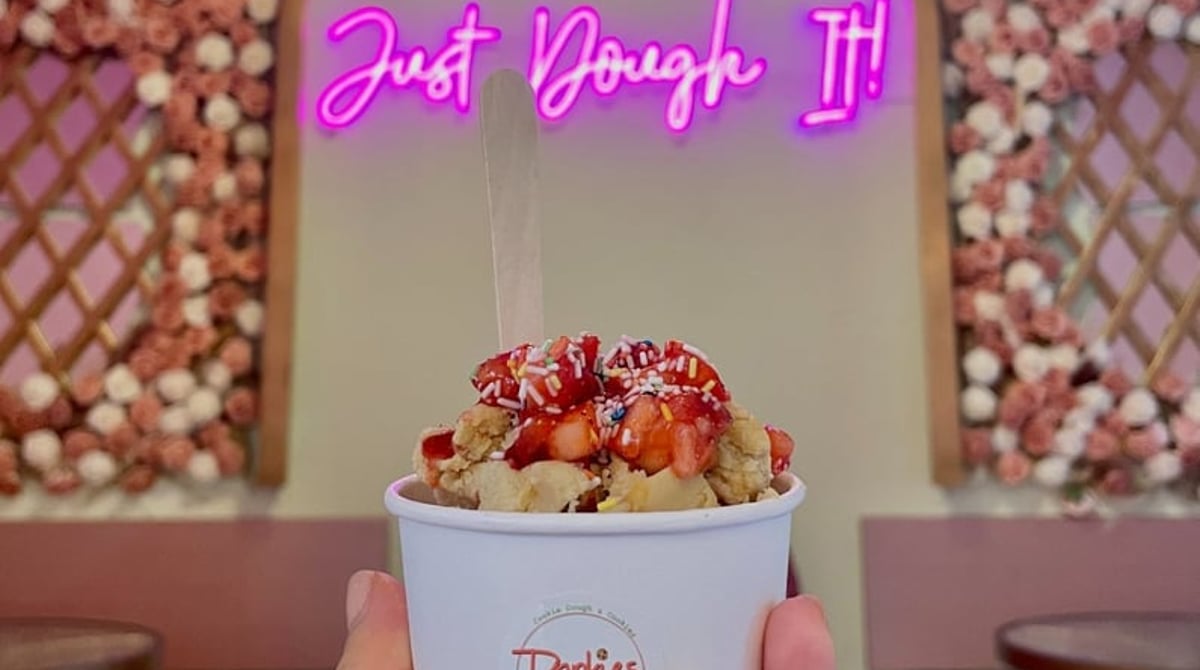 Becher mit Keksteig, Erdbeeren und Streuseln vor dem pinkfarbenen Neonschriftzug „Just Dough It!“