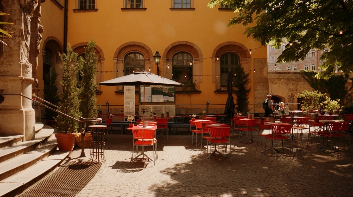 Sonnige Terrasse der Rustikeria im Hof des Müller'schen Volksbads in München-Haidhausen mit roten Tischen und Stühlen