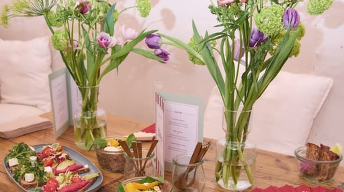Holztisch mit Blumensträußen, Salatplatte und kleinen Schalen vor einer Sichtbackstein-Wand