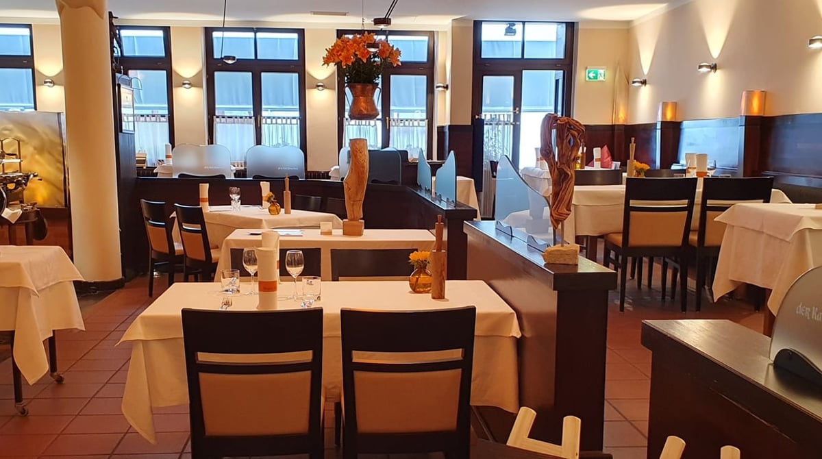 Gastraum der Osteria der Katzlmacher mit gedeckten Tischen, Holzskulpturen und Fenstern zur Straße