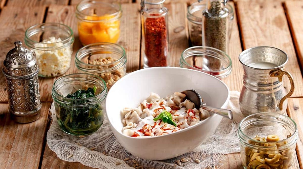 Schale mit Manti, Joghurt und Zutaten in Gläsern auf einem Holztisch