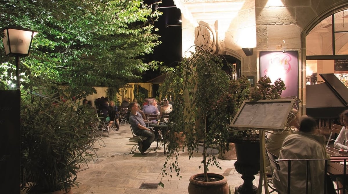 Abends beleuchteter Garten des Cafés am Beethovenplatz mit Tischen zwischen Bäumen und Pflanzen
