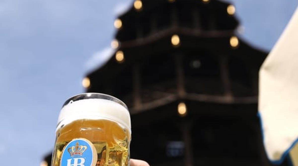 Eine Hand hält eine Maß Hofbräu vor den Chinesischen Turm