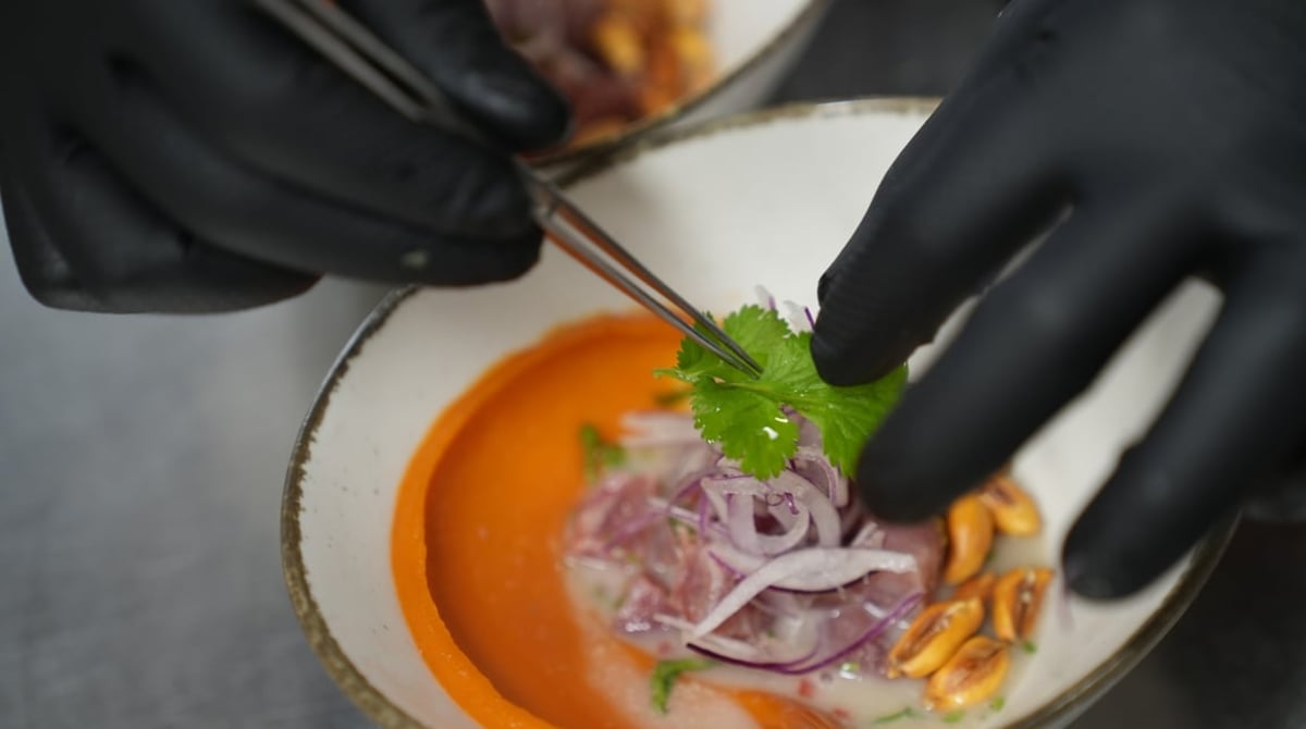Ceviche wird in der Küche des Nasca mit Koriander angerichtet, darunter eine orange Ají-Creme und Cancha