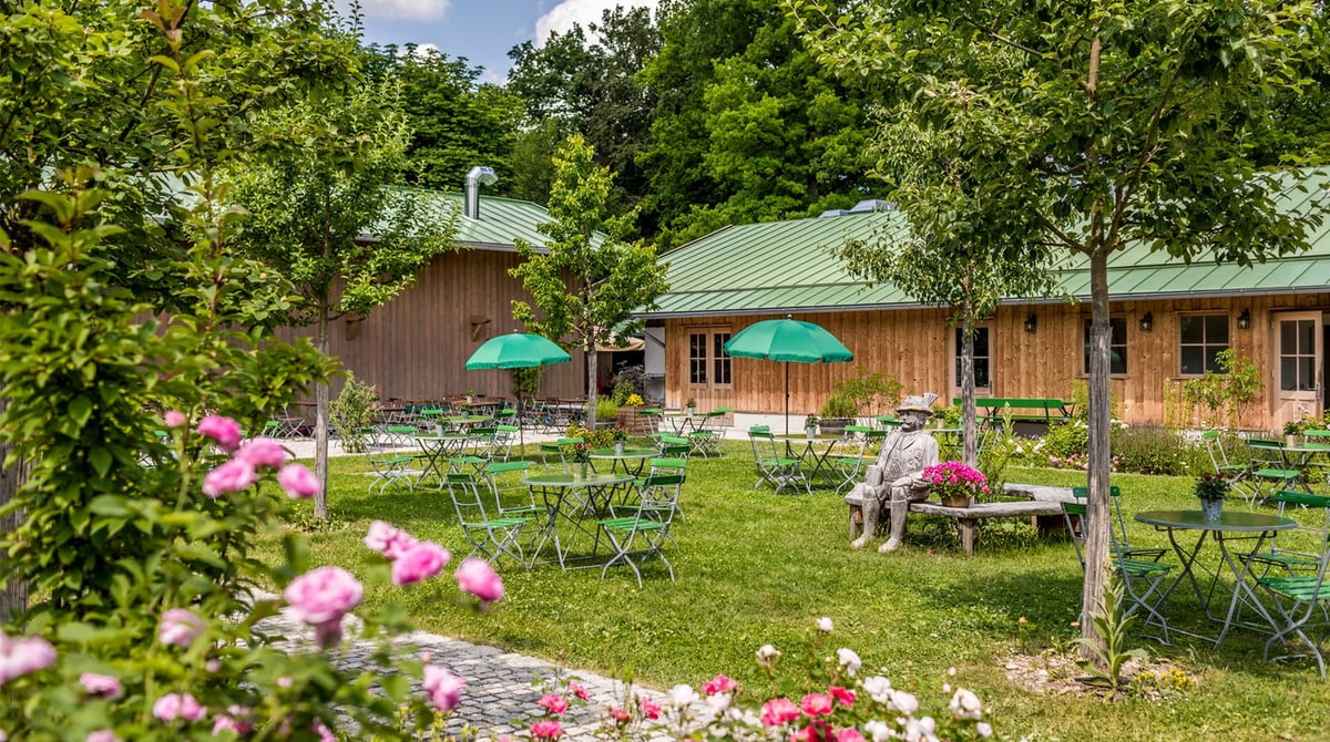 Obstgarten der Kugler Alm mit kleinen Tischen, grünen Schirmen und Pfingstrosen