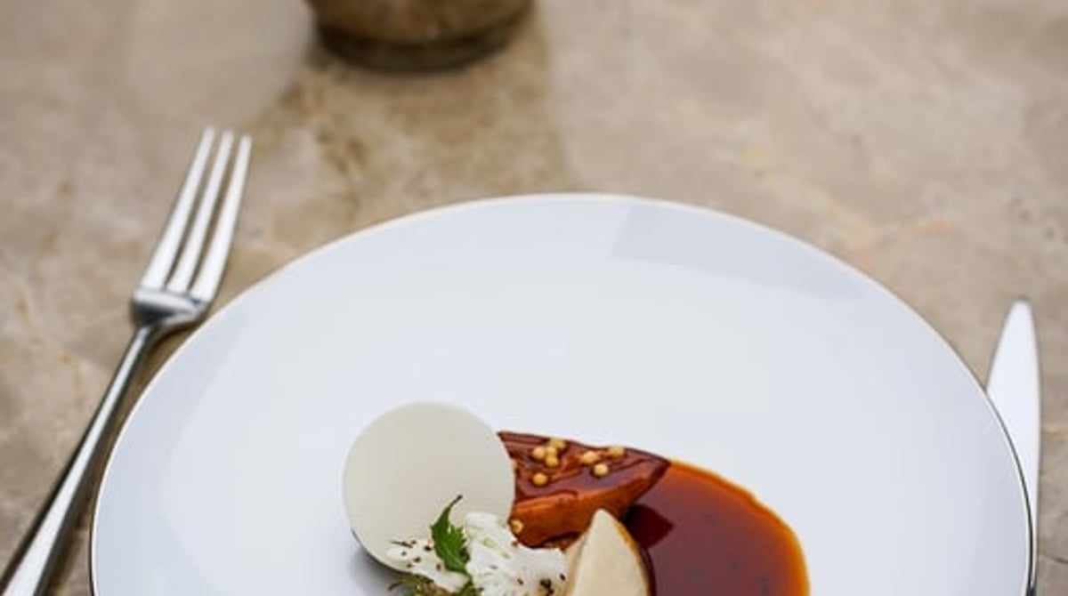 Dessert mit Sauce auf einem weißen Teller, daneben eine kleine Kanne