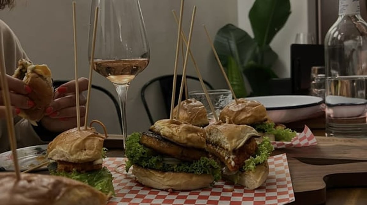 Gedeckter Tisch mit Burgern auf rot-weiß kariertem Papier und Weingläsern