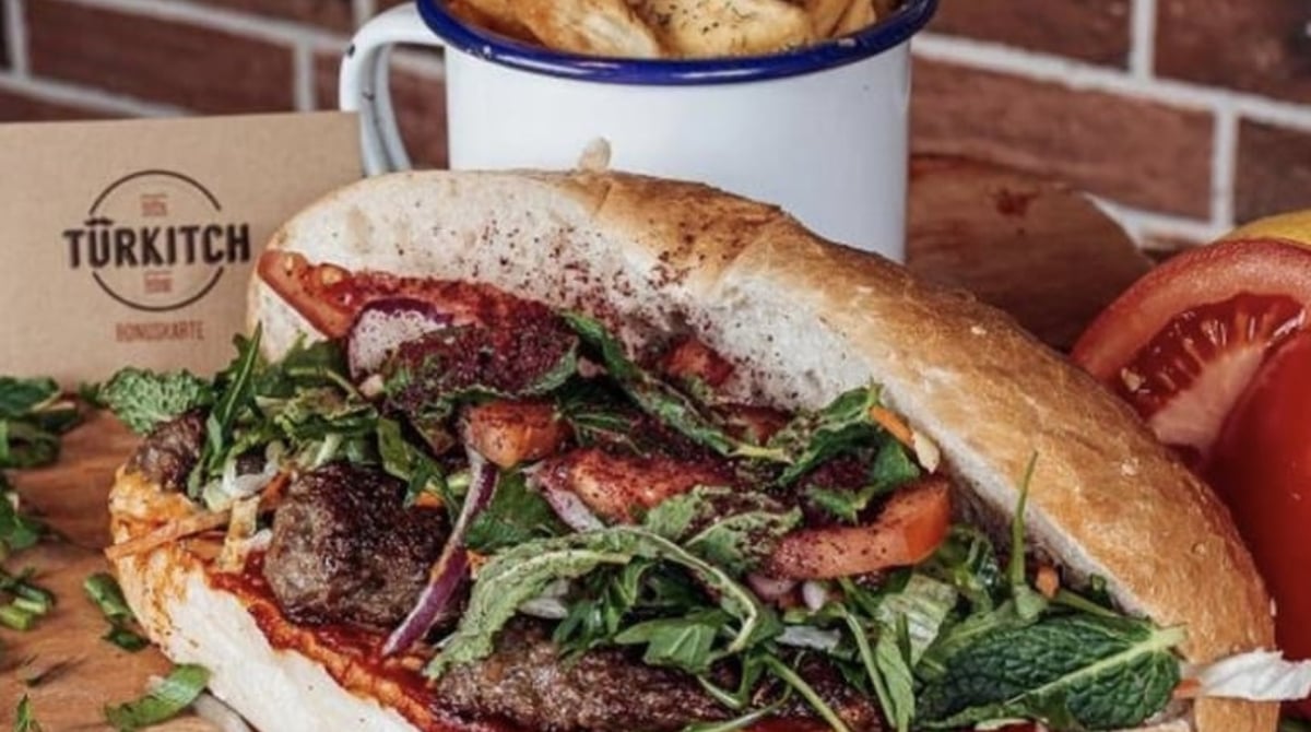 Köfte im Brot mit Rucola und Tomate, daneben Pommes im Emaillebecher von Türkitch
