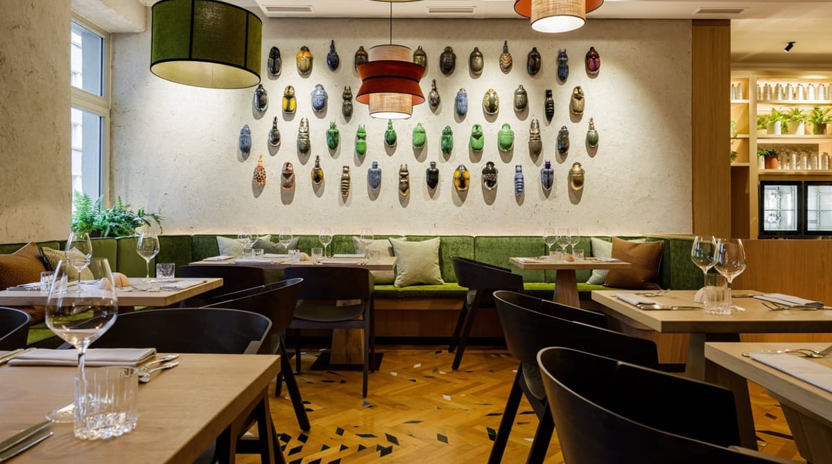 Gastraum des Beetle in München-Bogenhausen mit grüner Polsterbank, Holztischen und einer Wand voller glasierter Käfer