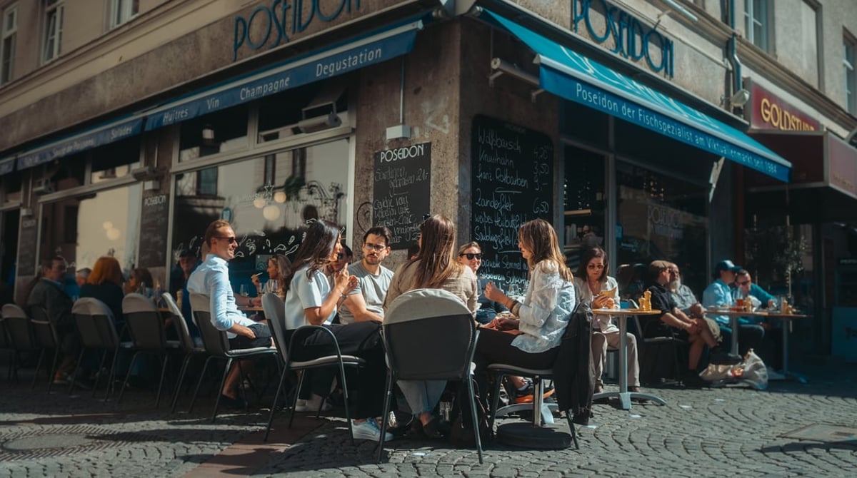 Eckhaus des Poseidon mit blauen Markisen und voll besetzter Terrasse auf dem Kopfsteinpflaster