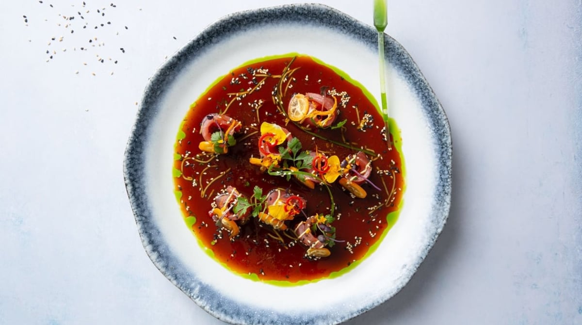 Thunfisch-Tiradito in dunkler Sauce mit Blüten auf einem hellen Teller, von oben fotografiert