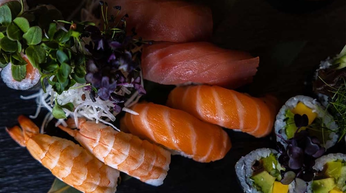Nigiri mit Lachs, Thunfisch und Garnelen sowie Maki mit Avocado und Mango auf einem schwarzen Teller im RYU