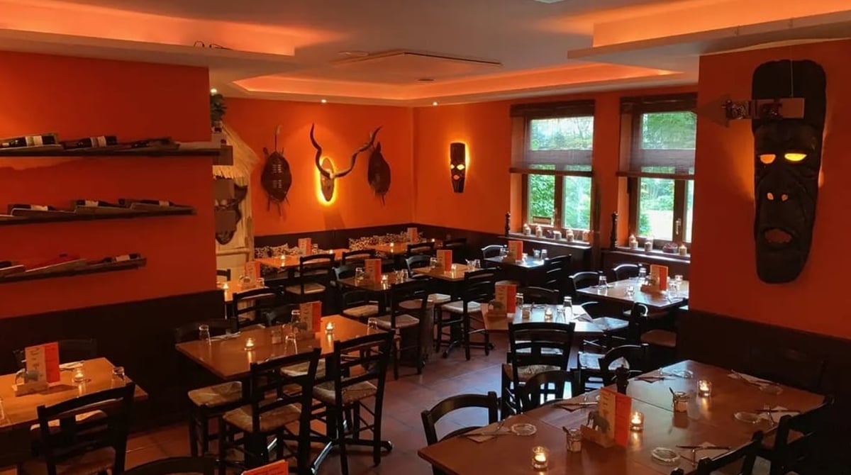 Gastraum des Savanna Grill mit orangefarbenen Wänden, Holztischen und afrikanischem Wandschmuck