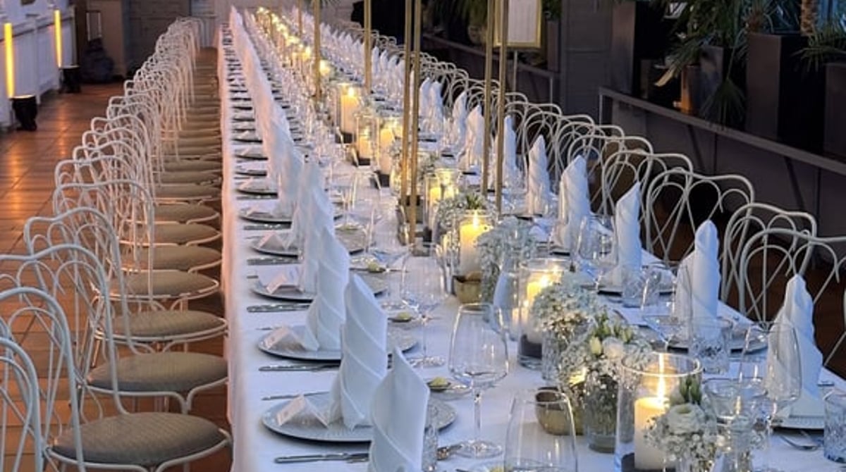 Lange gedeckte Tafel mit Kerzen und Blumen in der Glashalle des Palmenhauses