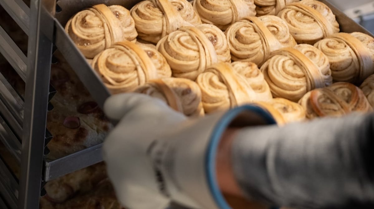 Blech mit frisch gebackenen Cardamom Buns, das ein Bäcker mit Handschuh aus dem Ofenwagen zieht