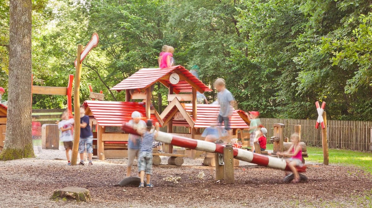 Holzspielplatz der Kugler Alm mit spielenden Kindern unter Bäumen