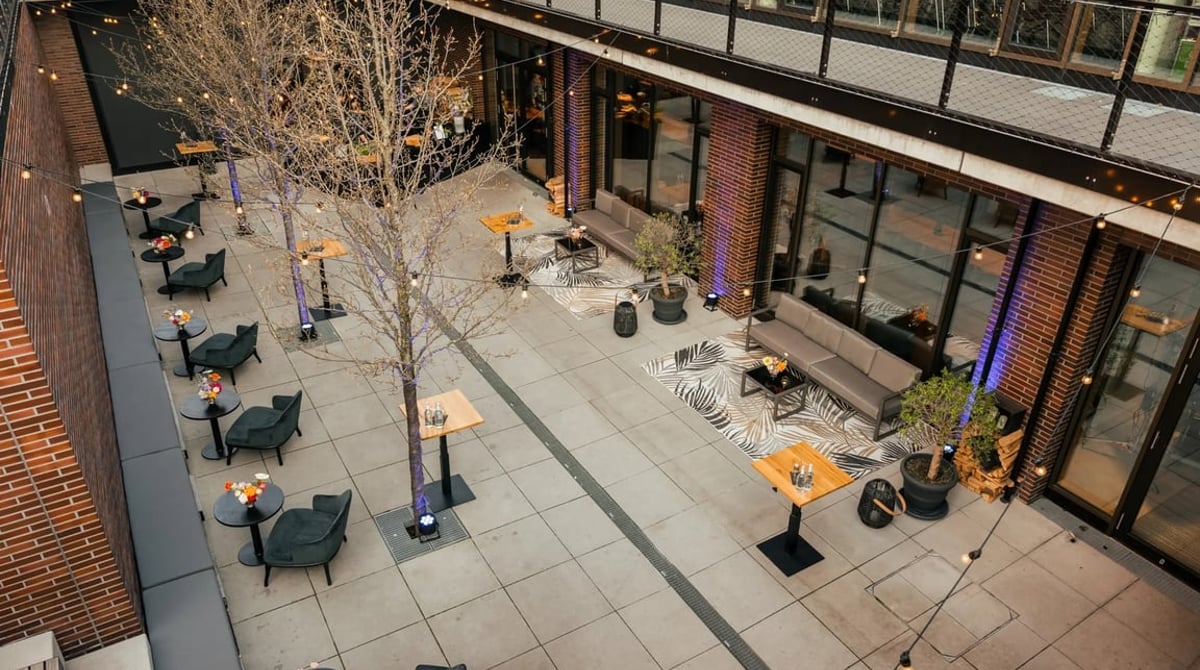 Terrasse des Y.OUR Pavillons in München-Schwabing mit Tischen, Sesseln und Lichterketten im Innenhof