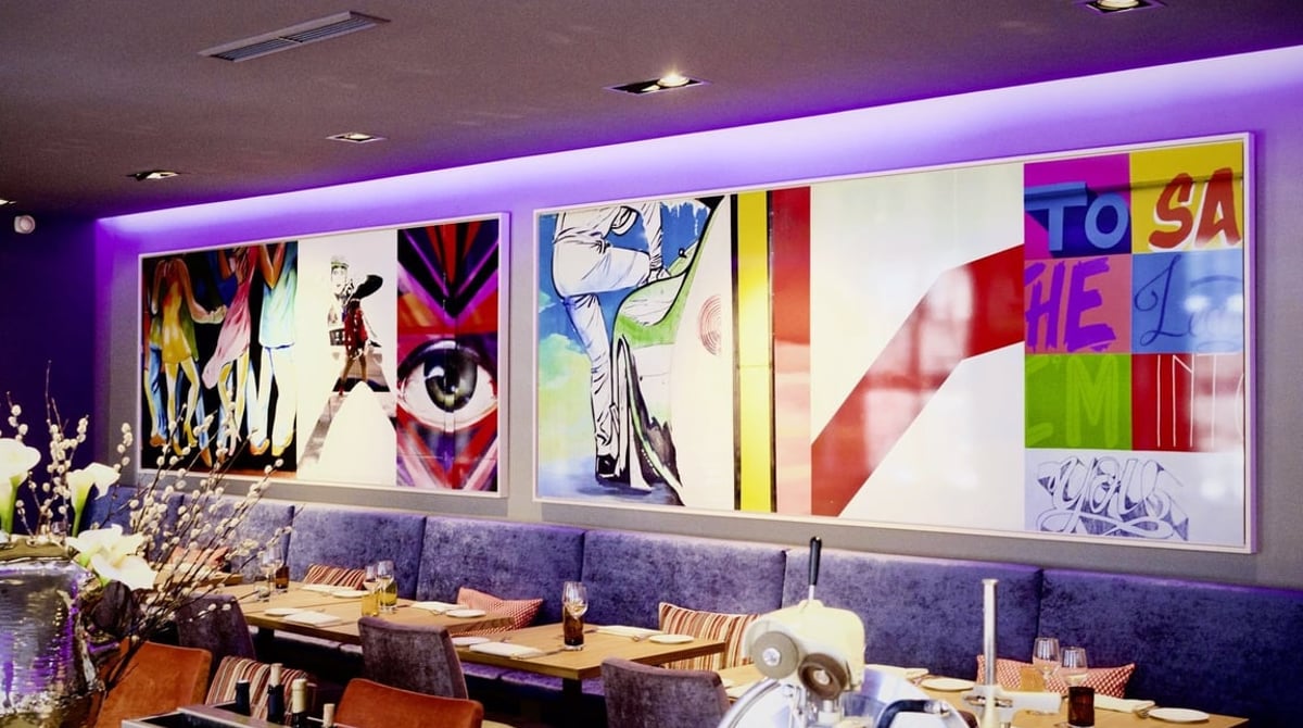 Gastraum des Blauen Bocks mit blauen Polsterbänken, gedeckten Holztischen und großen bunten Pop-Art-Bildern an der Wand