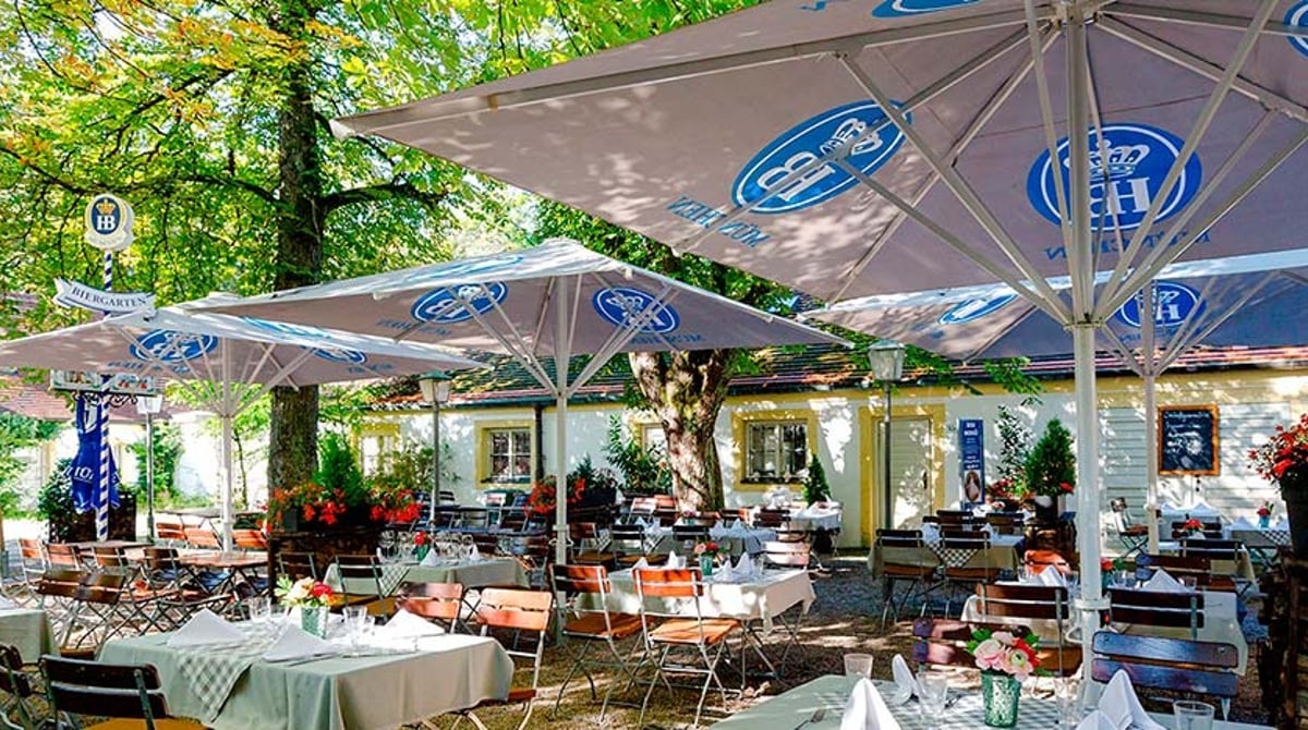 Gedeckte Tische und Hofbräu-Sonnenschirme unter Kastanien im Schlossbiergarten der Schlosswirtschaft Schwaige