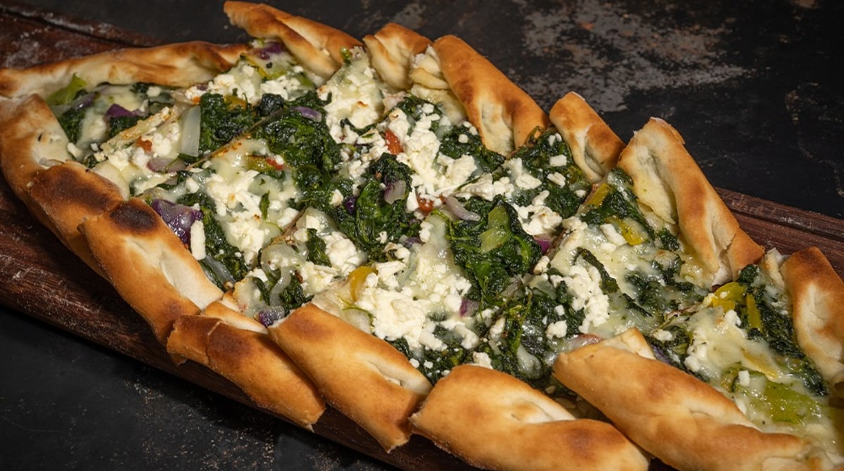 Pide mit Spinat und Schafskäse auf einem Holzbrett