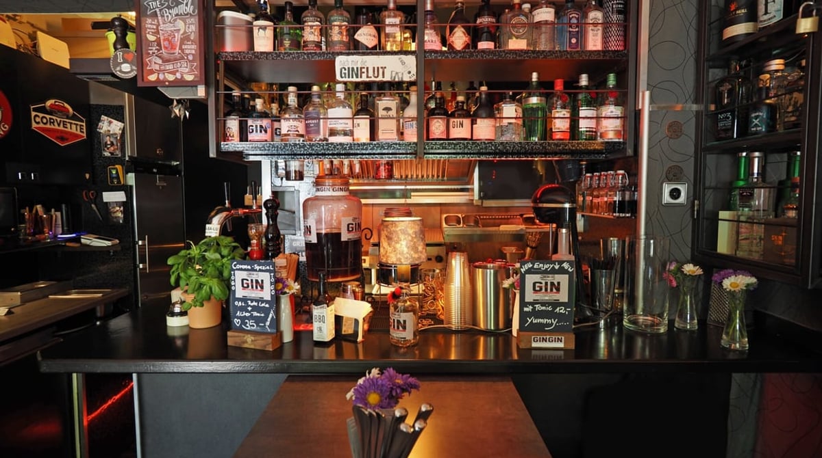 Bar des CA-BA-LU mit Gin-Flaschen, Spirituosenregal und Blumen auf dem Tresen