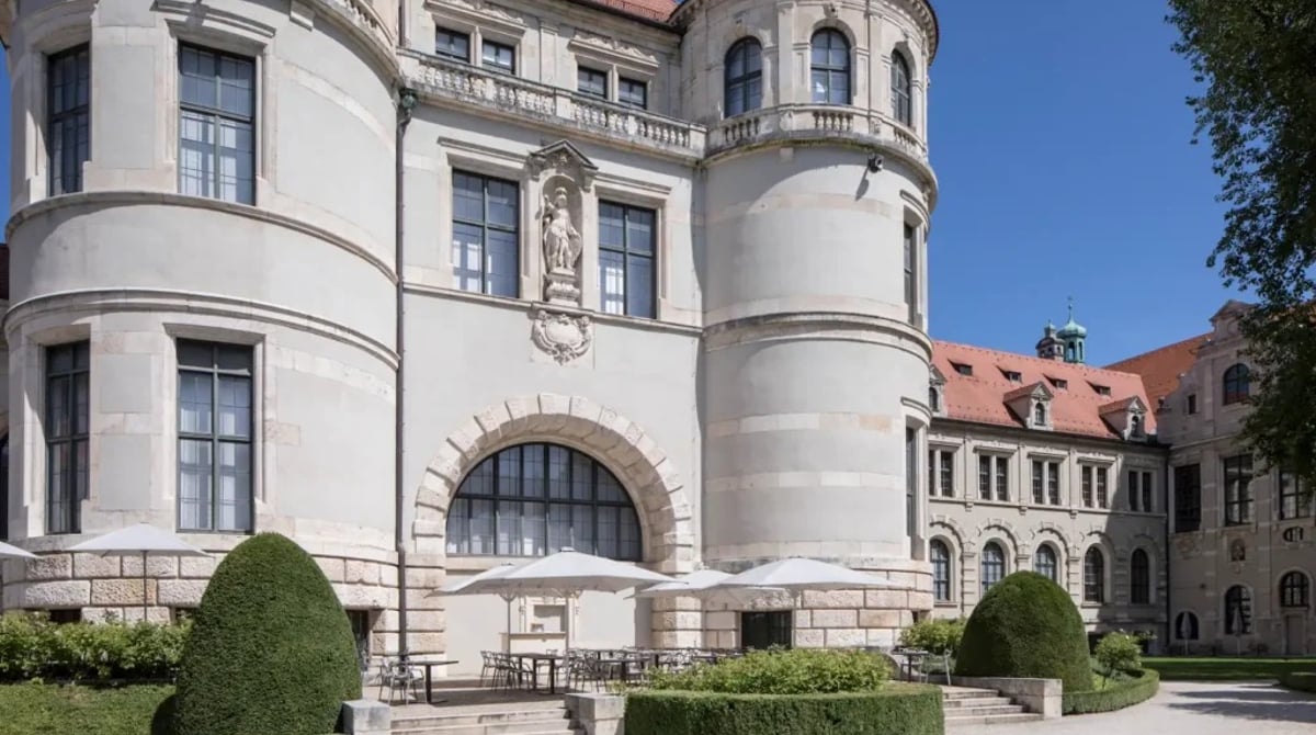 Gebäude des Bayerischen Nationalmuseums mit Rundturm, davor Hecken und die Terrasse