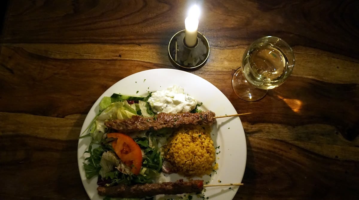 Spieße mit Salat und Reis neben Kerze und Weißwein in der Yol Taverne