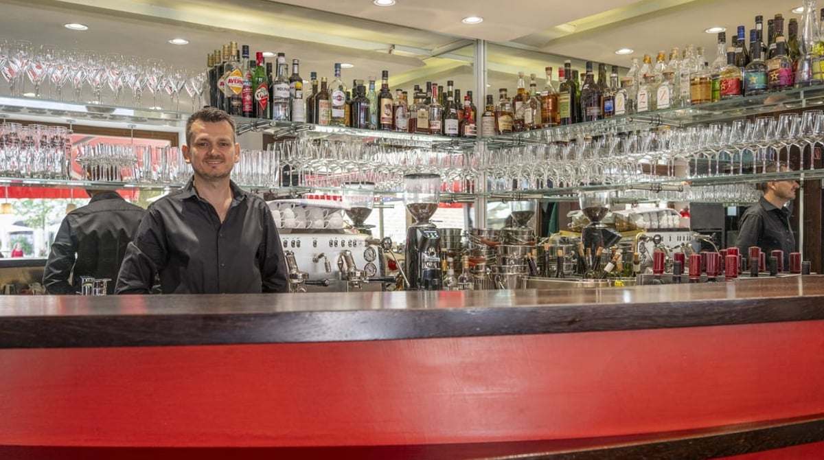 Geschwungene rote Bar mit Flaschenregal, dahinter ein Mitarbeiter