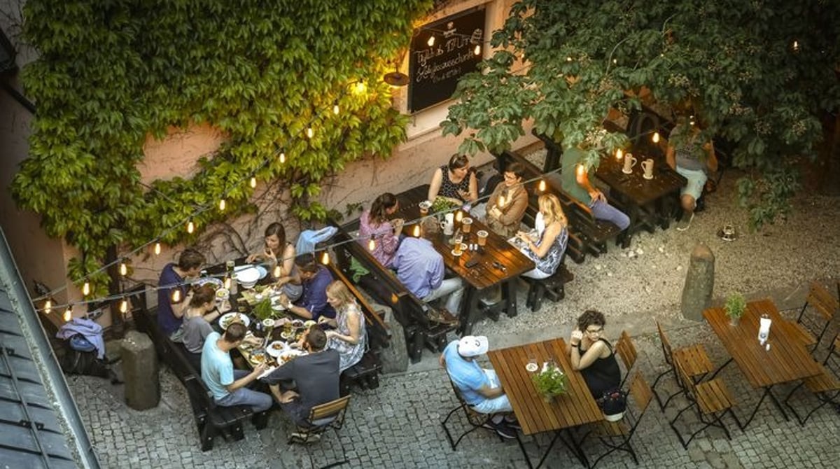 Wirtsgarten des Ayinger in der Au am Abend mit Lichterketten und Gästen an Holztischen