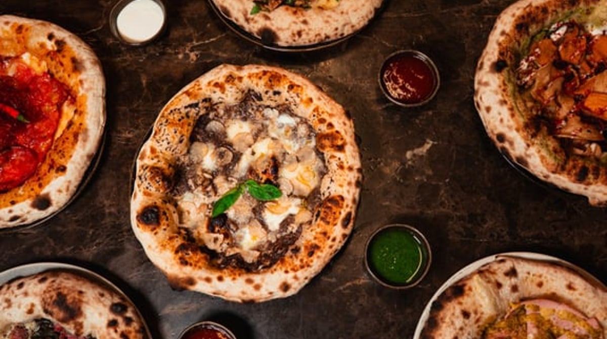 Mehrere neapolitanische Pizzen von oben auf einem dunklen Tisch