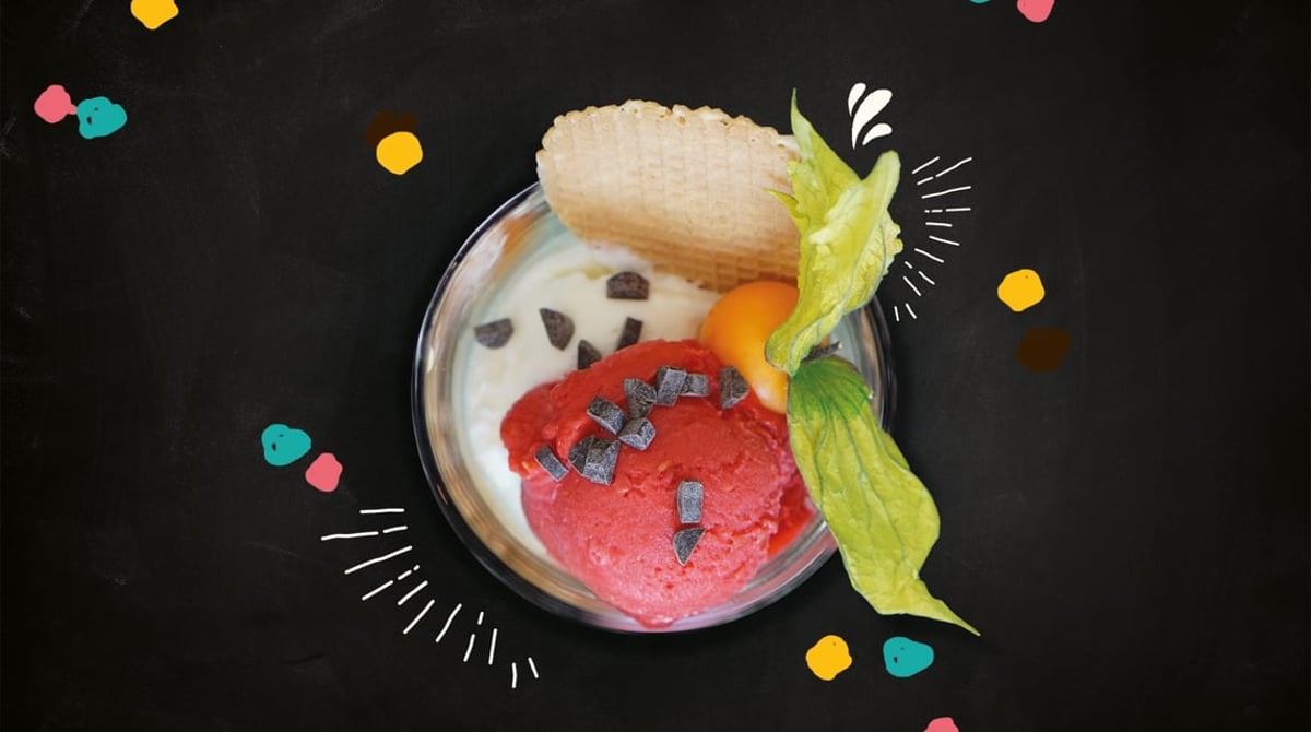 Eisbecher mit Kugeln, Waffel, Schokostückchen und Physalis, von oben fotografiert auf dunklem Grund