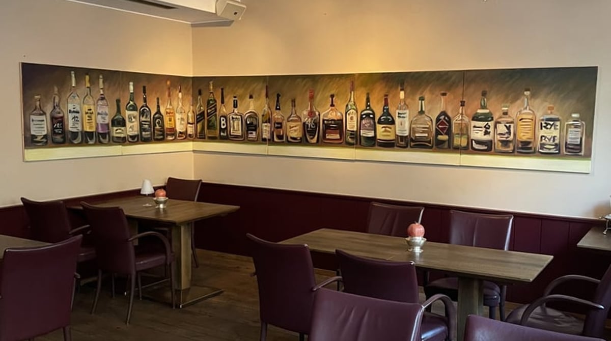 Sitzecke im Restaurant Ederer mit Bänken, Holztischen und einem langen Bild mit Flaschen an der Wand
