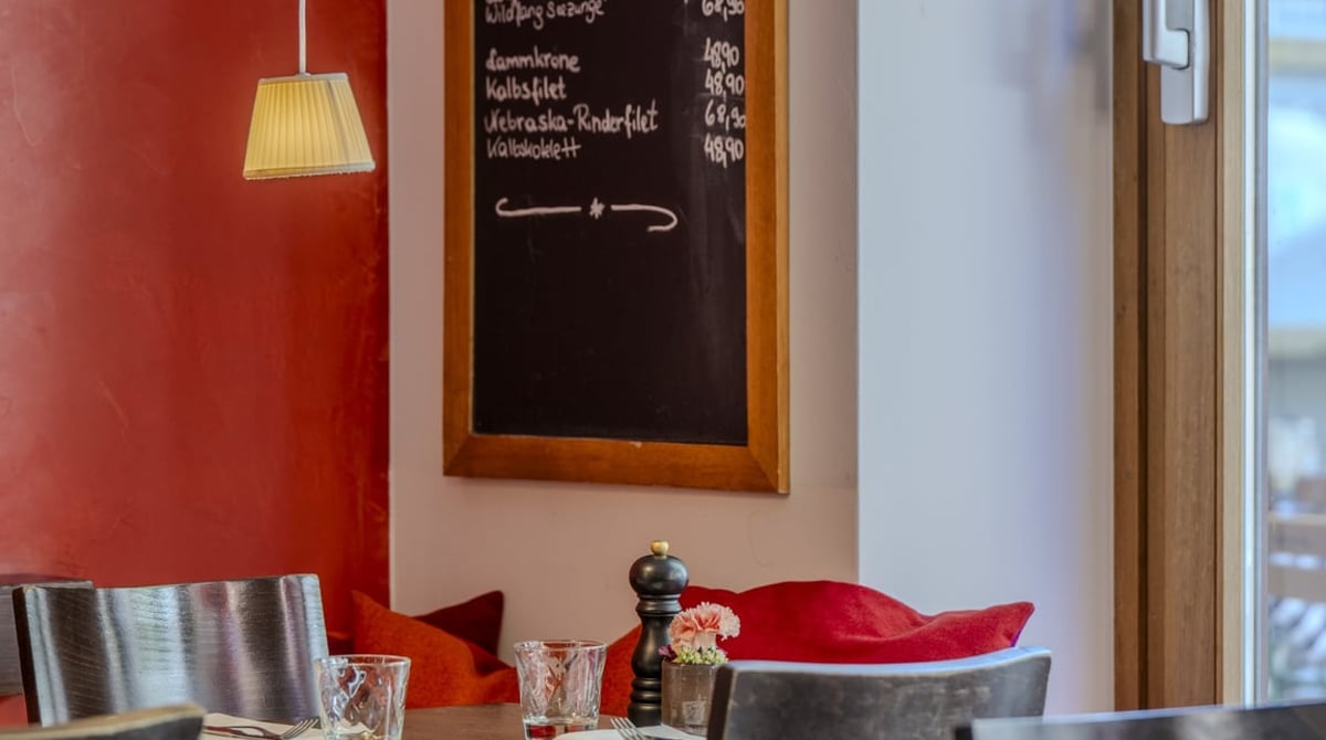Roter Gastraum mit Tafel, auf der die Tagesgerichte stehen, und gedecktem Tisch