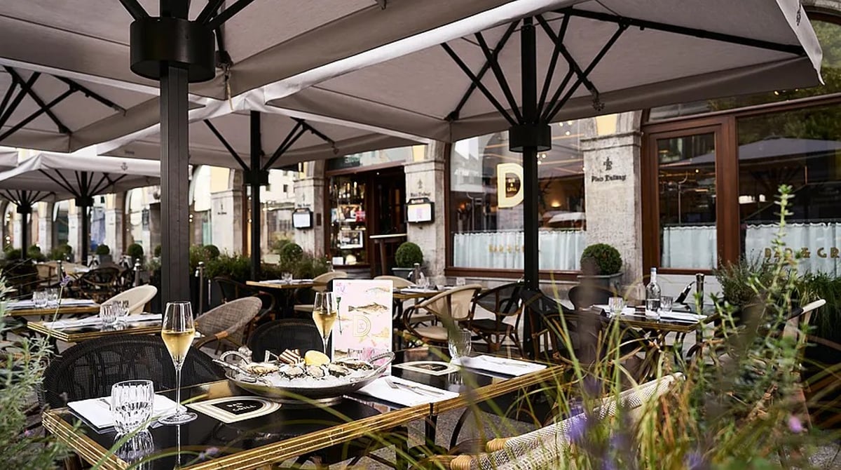Terrasse der Dallmayr Bar & Grill unter großen Schirmen mit gedeckten Tischen und Pflanzen
