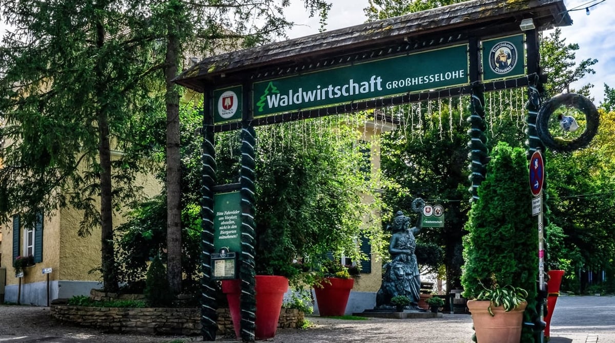 Eingangstor „Waldwirtschaft Großhesselohe“ mit grünem Dach und Blumen