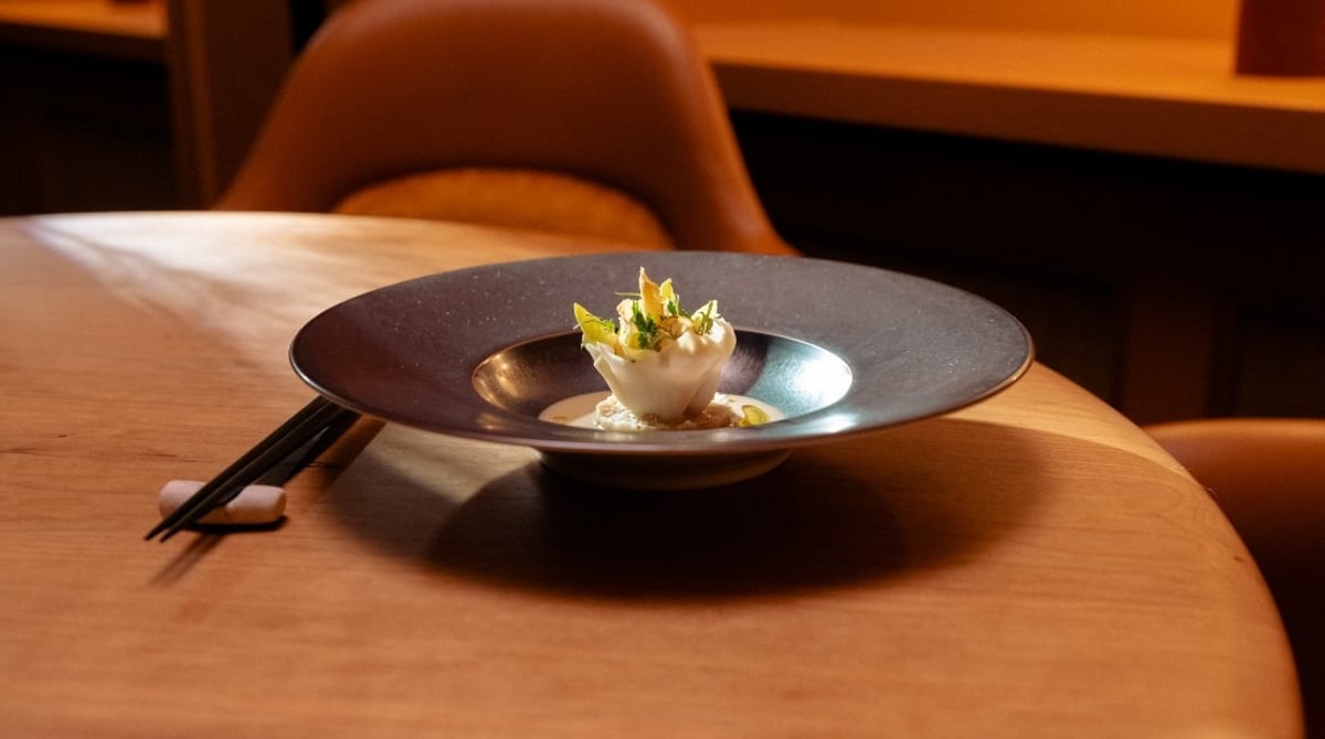 Gericht in dunkler Schale mit Essstäbchen auf einem Holztisch