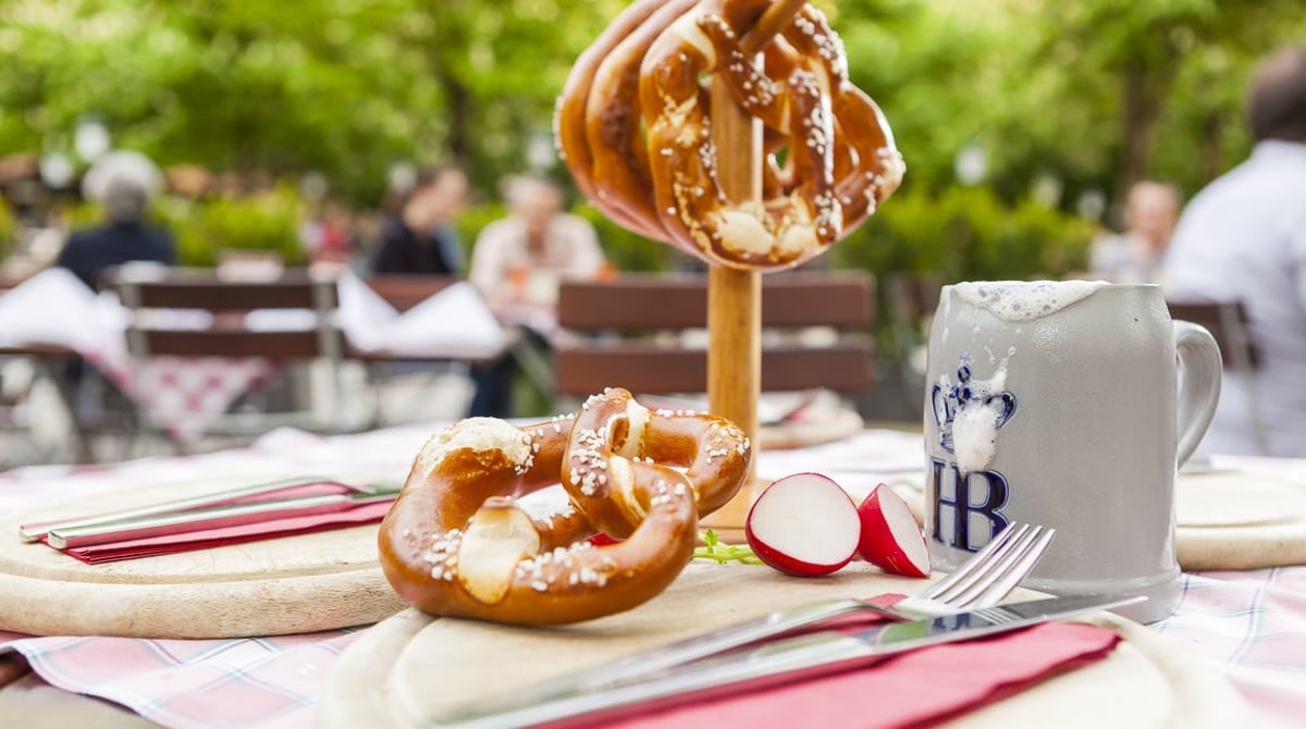 Brotzeit mit Breze im Biergarten, daneben ein Hofbräu-Krug