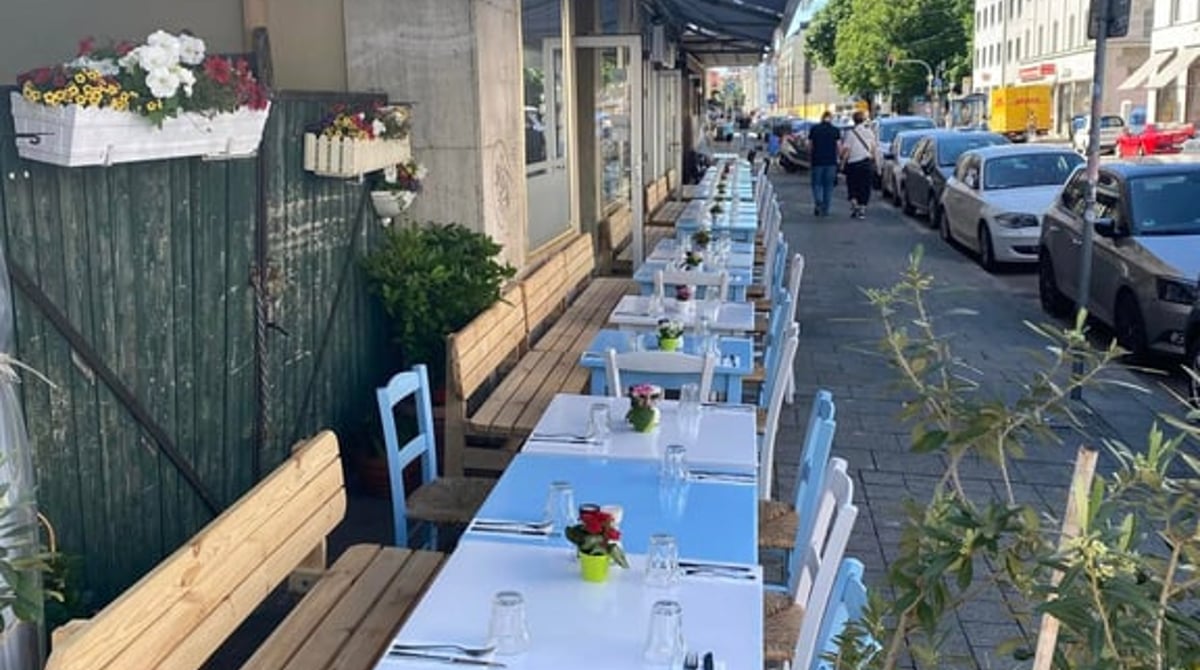 Gedeckte Tische mit Stühlen unter der Markise am Gehweg vor dem Kreta Grill