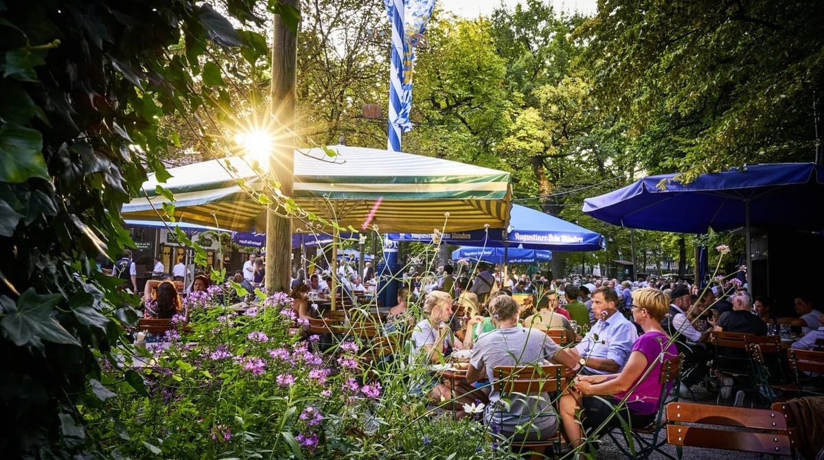 Gäste unter Sonnenschirmen und Kastanien im Biergarten des Augustiner-Kellers im Abendlicht
