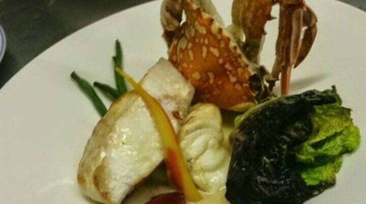Fischgericht mit Krustentier und Gemüse auf einem weißen Teller
