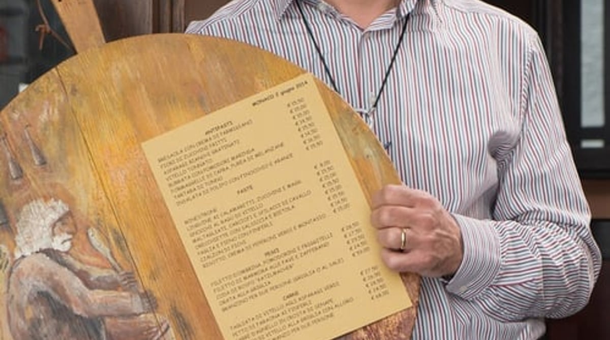 Giorgio Cherubini hält eine bemalte Holztafel mit der Speisekarte