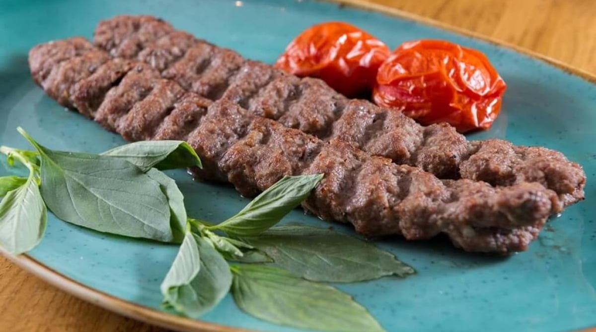 Gegrillter Hackfleischspieß mit Tomaten und Basilikum auf türkisfarbenem Teller im Tahdig