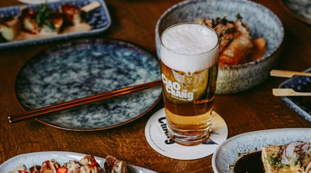 Gedeckter Holztisch mit mehreren kleinen Tellern, einem Glas Bier und Stäbchen