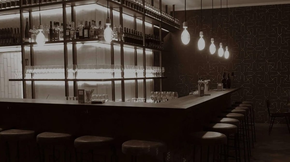 Bar mit beleuchtetem Regal, Gläsern und Pendelleuchten im Weinheim